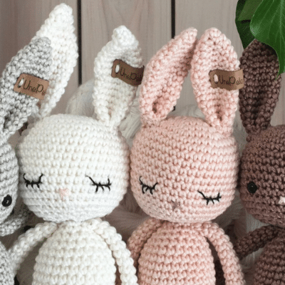 quatre lapins en coton conçus au crochet. Les lapins sont gris, blanc, rose et marron